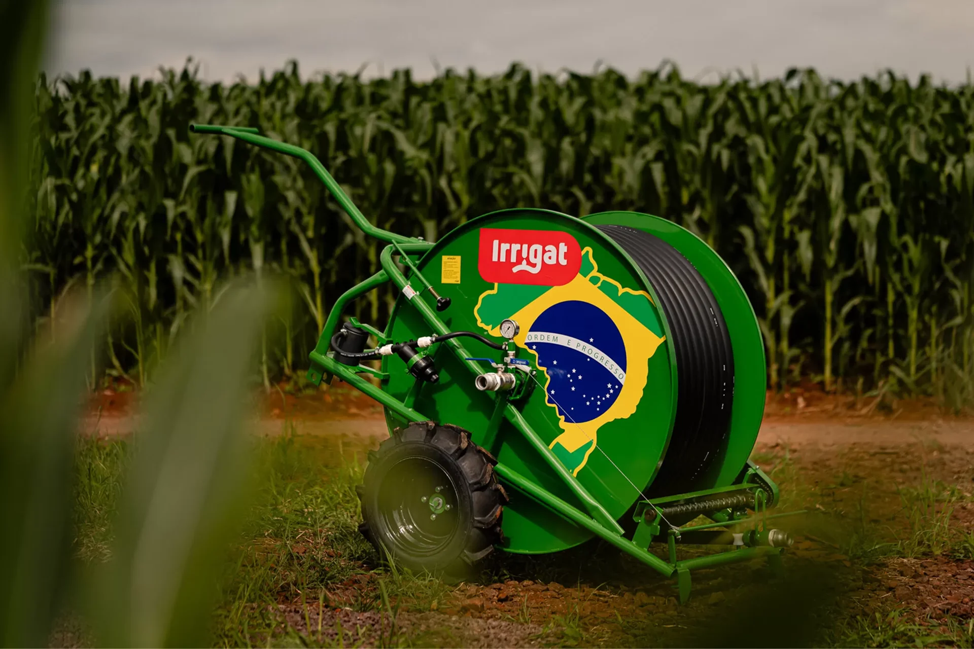 A imagem apresenta um carretel Irriat 50/120 versão Brasil em frente a uma lavoura de milho